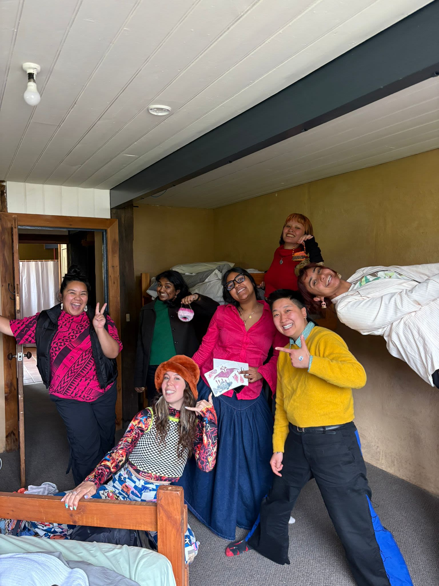 Seven people are posing for a photo in the bunkroom. They are smiling and laughing.