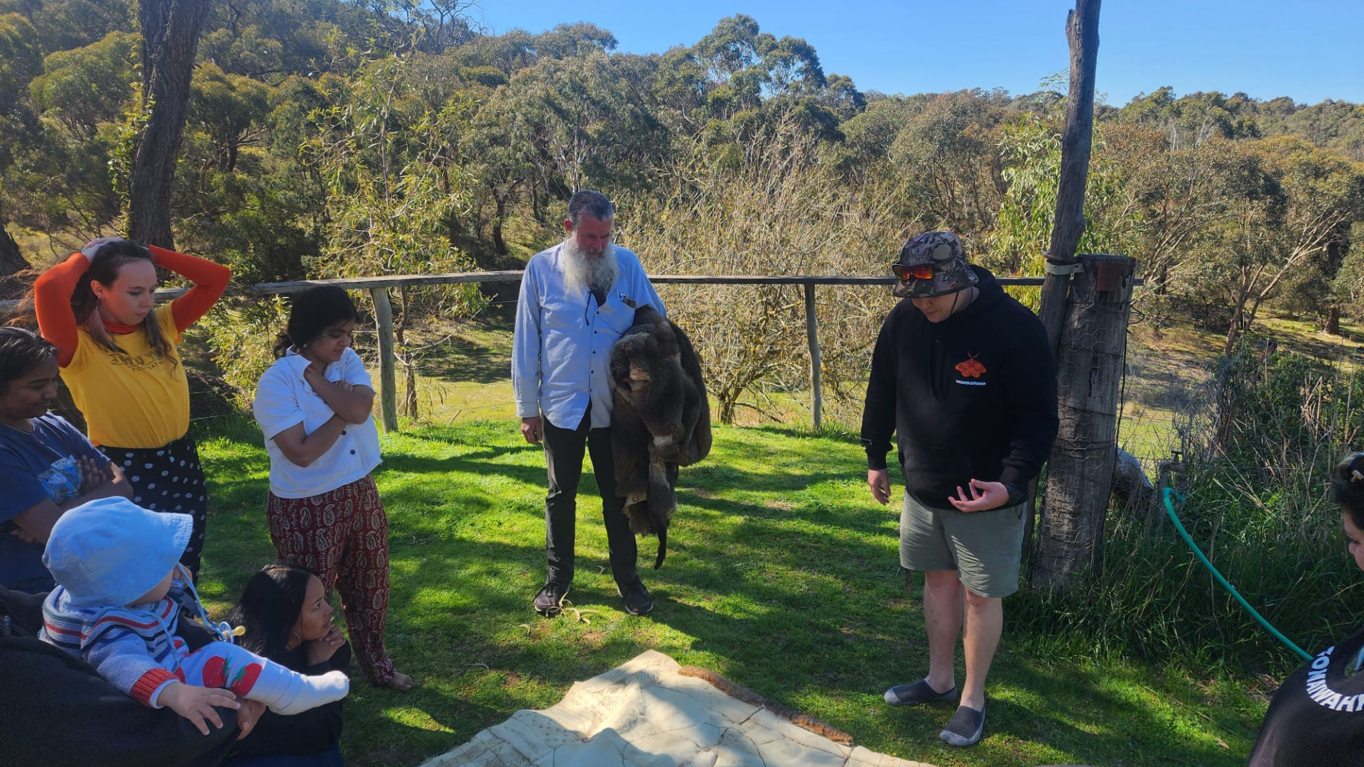 People gathered around a possum cloak which lays on the ground.