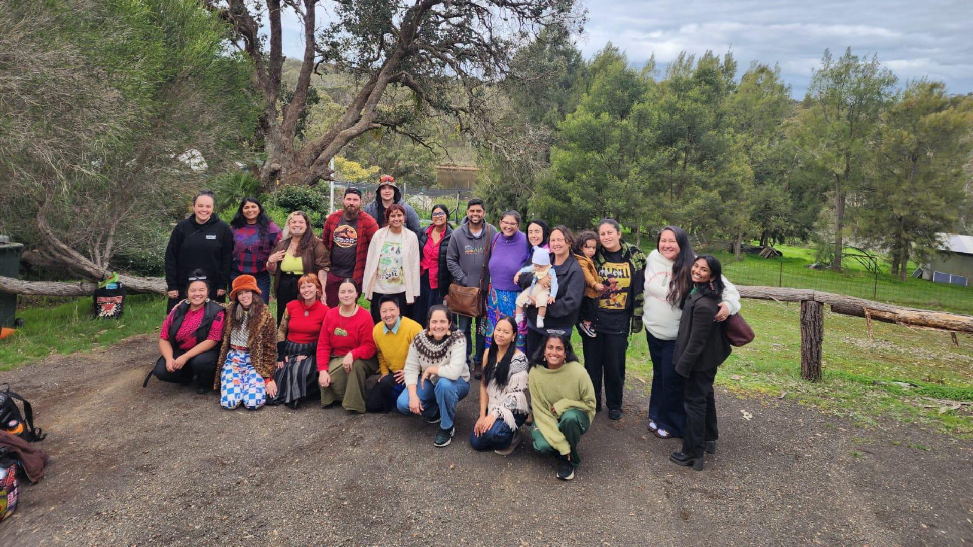A group of 24 or so people looking at the camera with lush green trees in the background.