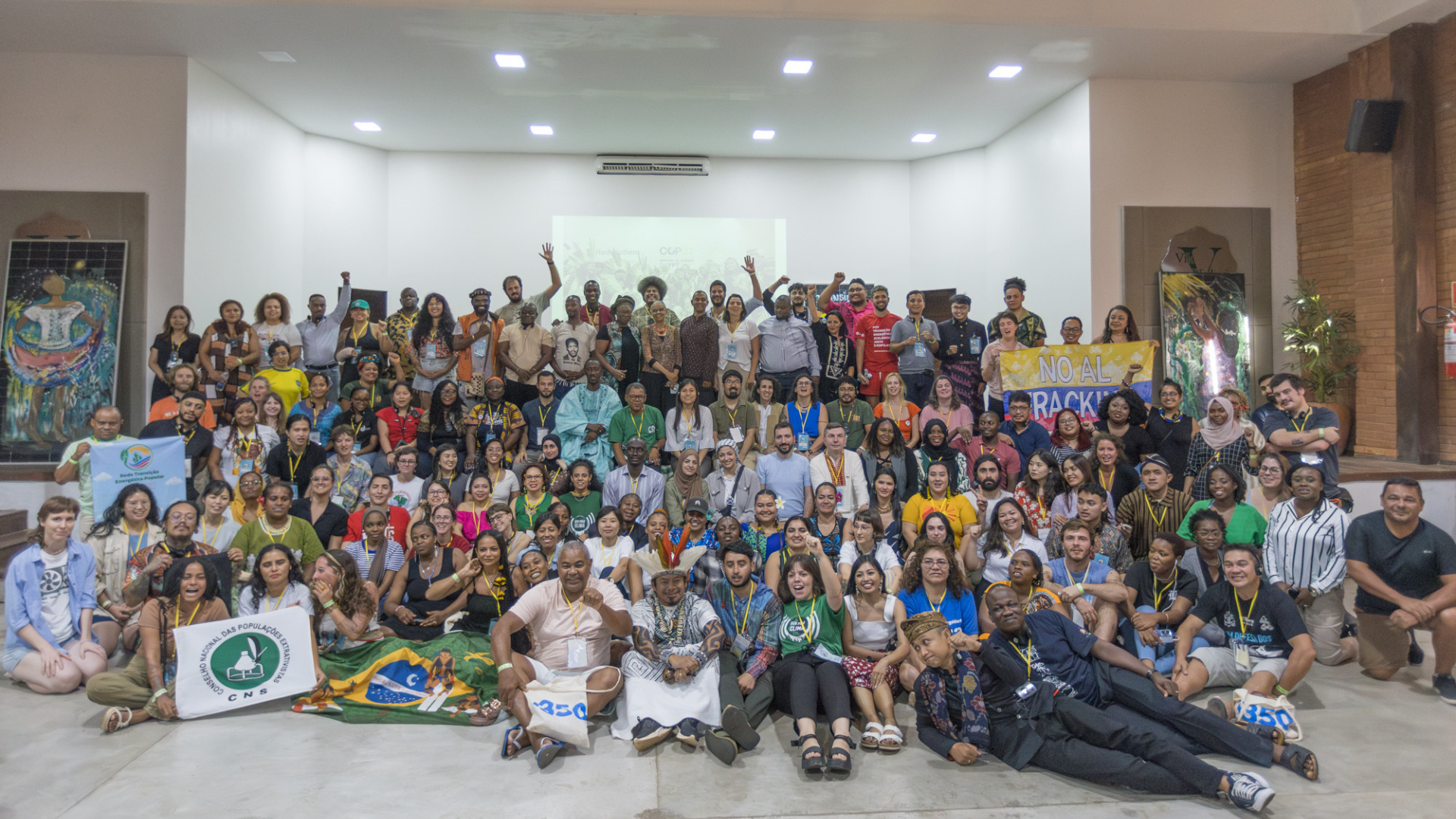 A large group of people gathered indoors for a group photo, with some holding banners and flags.