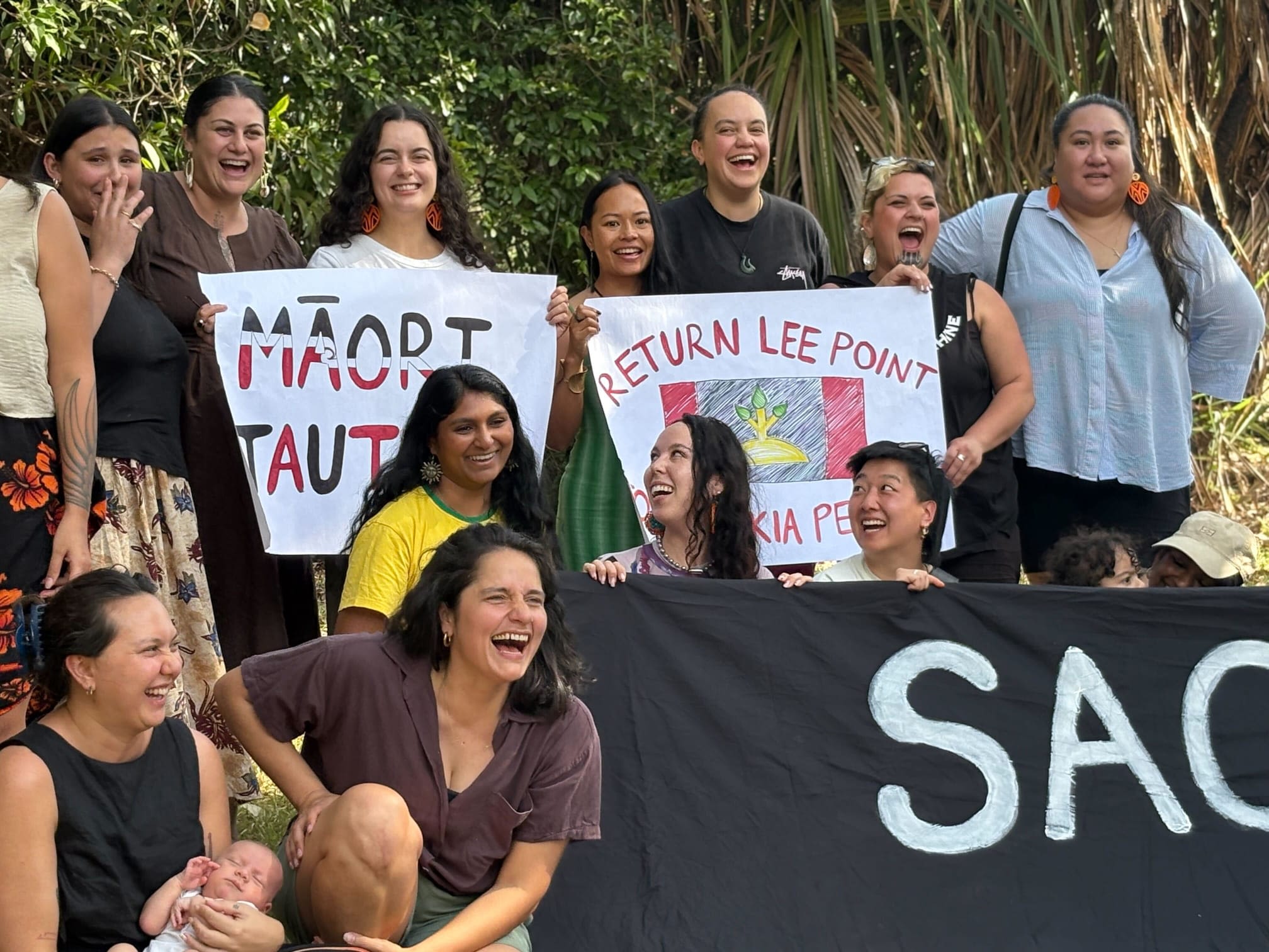 A close up photo of some of the participants in the cohort laughing and holding signs of solidarity with Lee Point.