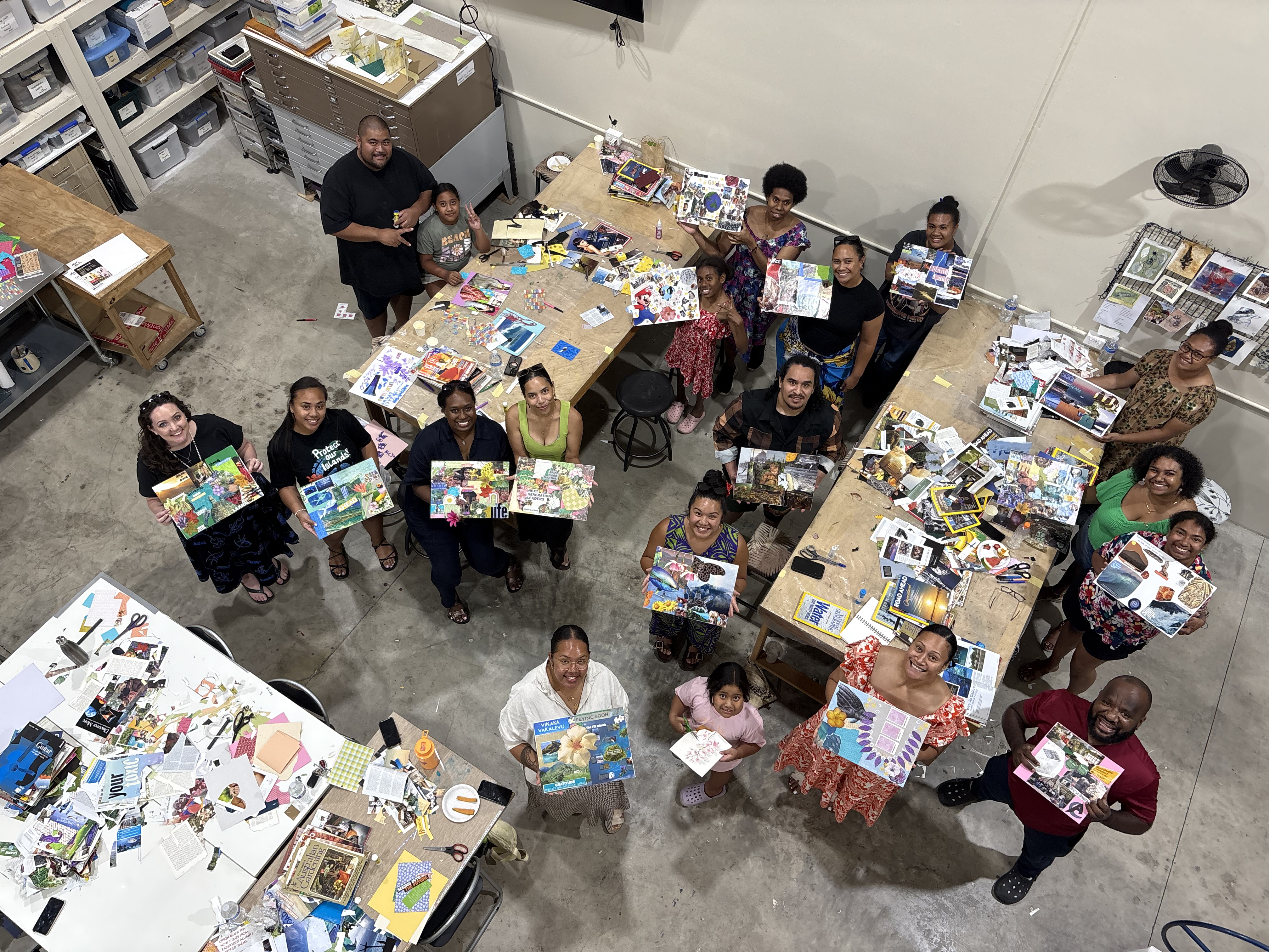 The photo is taken from above. A group of around 20 First Nations and Pasifika people are holding their collages and looking at the camera smiling